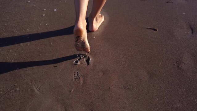 Young woman feet walk along wet sand near sea waves edge