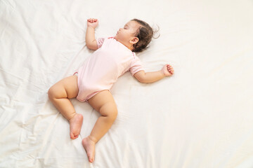 Healthy little baby girl infant wearing pink cloth sleeping calm peaceful relax on white bed at home. Adorable one year old toddler mixed race asleep having good dream resting in the bedroom.Lifestyle