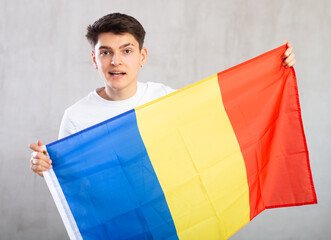 Reliant positive young man holds big national flag of Romania with confident smile showing teeth....