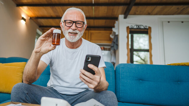 senior man sit at home hold bottle medicine pills drugs and smartphone