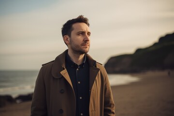 Portrait of handsome young man in coat on the beach at sunset