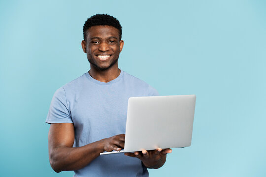 Portrait of handsome smiling African computer programmer holding laptop isolated on blue background, successful business. Happy Nigerian student studying looking at camera, online education concept 