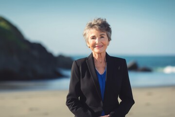 Fototapeta na wymiar Portrait of smiling senior businesswoman standing on beach with hands in pockets