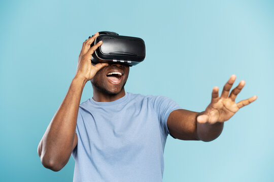 Portrait of handsome excited African American wearing VR glasses playing video game isolated on blue  background. Technology, innovation concept - Powered by Adobe