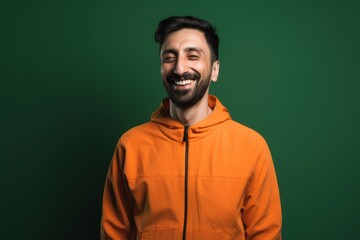 Fototapeta premium Portrait of a smiling young man in orange hoodie against green chalkboard