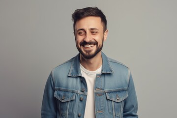 Obraz premium Handsome young man in denim jacket smiling and looking at camera while standing against grey background