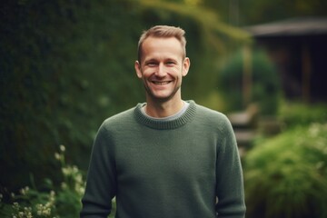 Portrait of a young handsome man in a green sweater standing in the garden.