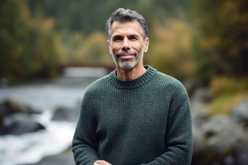 Portrait of a handsome middle-aged man in a sweater on the background of a mountain river.