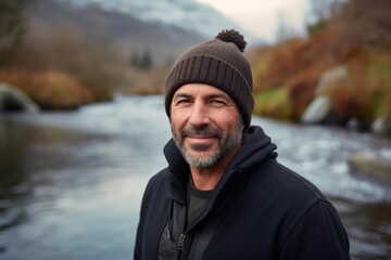 Handsome middle-aged man in a warm hat and jacket standing by a river.