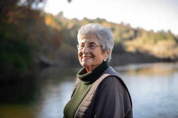 Fototapeta premium Portrait of happy senior woman standing on bank of river in autumn