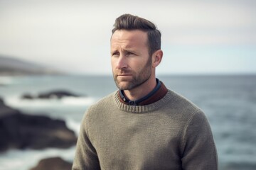 Portrait of a handsome man standing by the sea wearing a sweater