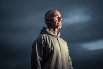 Mature bald man in sportswear looking away against stormy sky