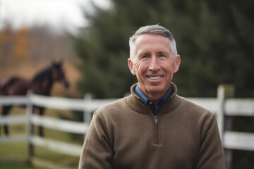 Portrait of smiling mature man standing with horse in background at ranch