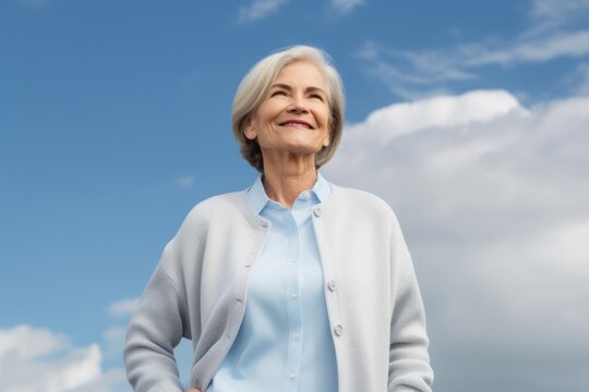 smiling senior woman with hands on hips over blue sky and clouds