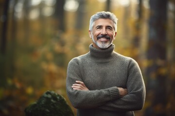 Portrait of a smiling senior man standing with arms crossed in autumn forest