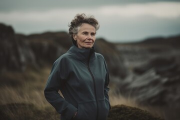 Portrait of senior woman standing on top of a mountain and looking at camera