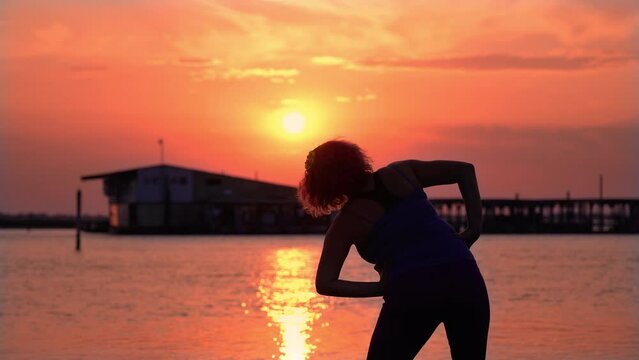 Plump woman does sports exercises on empty beach at sunset