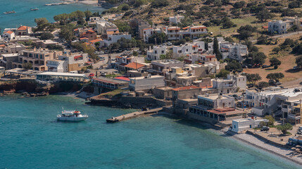 Fototapeta na wymiar Plaka, Elounda, Crete, Greece. 2023. Overview of the resort of Plaka and a small ferry boat inbound from the Fortress island of Spinalonga a former Leper Colony.