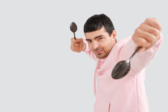 Young man with tablespoons on grey background