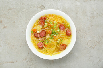 Delicious sauerkraut soup with smoked sausages and green onion on light grey table, top view