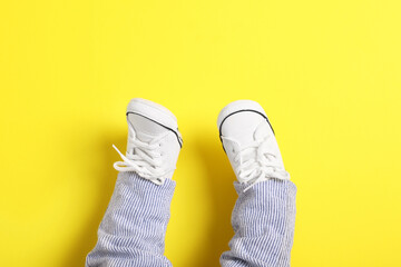 Little baby in stylish gumshoes on yellow background, top view. Space for text
