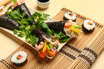Plate with tasty sushi cones, rolls, lambs lettuce and bamboo mat on color background, closeup