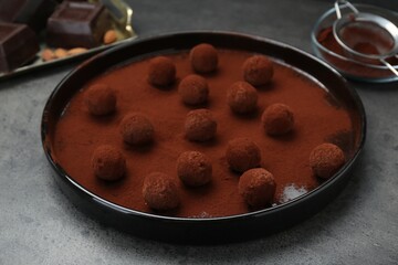 Delicious chocolate candies powdered with cocoa on grey table