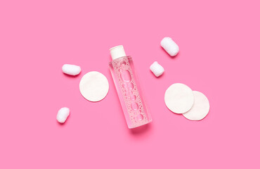Bottle of micellar water with cotton balls and pads on pink background