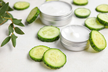 Jars of natural cream and cucumber slices on light background, closeup