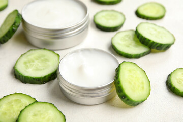 Jars of natural cream and cucumber slices on light background, closeup