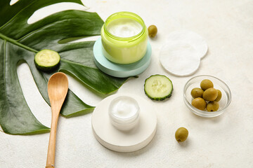 Composition with jars of natural cream, ingredients, cotton pads and palm leaf on light background