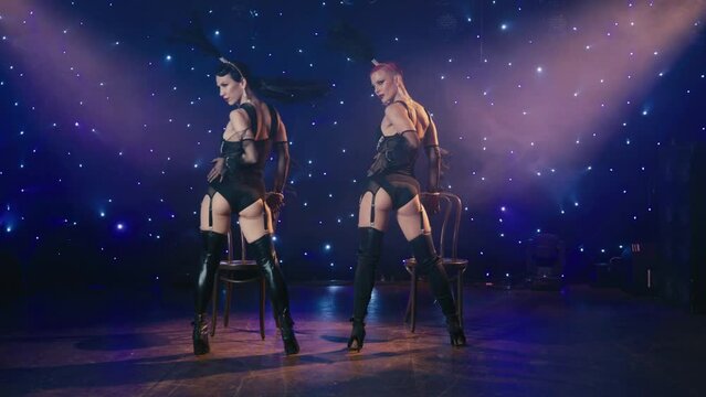 Passionate young sexy women captivating dance in black burlesque lingerie on theatre stage with night stars background in smoky spotlights. Cinematic purple lights on flirting seductive show girls 4K