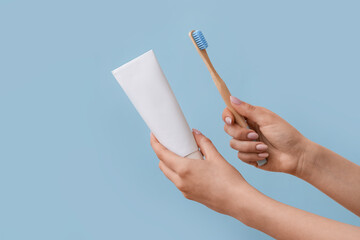 Female hand with bamboo toothbrush and paste on blue background