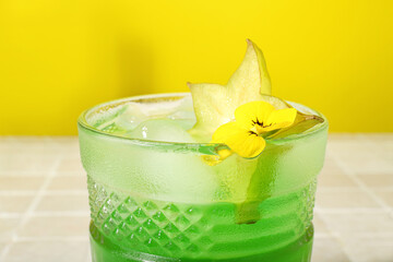 Fresh summer cocktail with carambola on tile table near yellow wall
