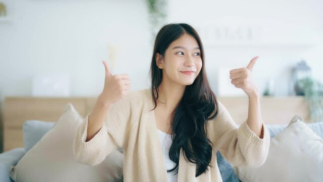 Happy teen asian girl blogger smiling face waving hand talking to webcam recording vlog, social media influencer streaming, making video call at home. She thumb up good or better