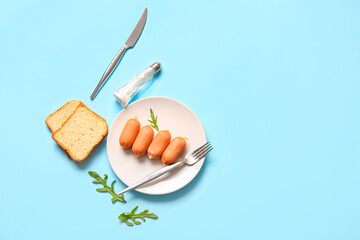 Plate of tasty boiled sausages with bread and arugula on blue background
