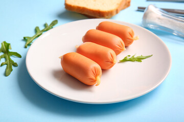 Plate of tasty boiled sausages with bread and arugula on blue background