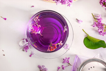 Glass cup of tea with lilac flowers on light table