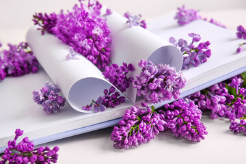 Composition with book and beautiful lilac flowers on light background, closeup