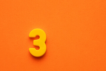 Number three yellow plastic - plastic digit on orange foamy background