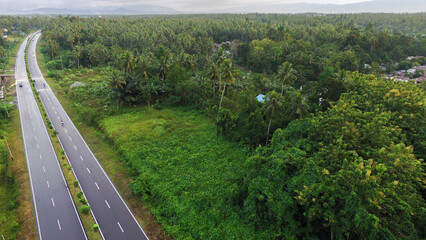 Aerial photo of the highway dividing the forest and villages with a mountain background.