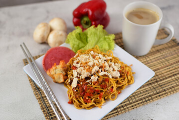 Mie goreng, Spicy fried noodle with chicken and chilli on topping served with a cup of coffee and vegetable in grey and texture backgound