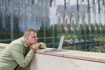 Sad guy with hearing aid using laptop outdoors. 