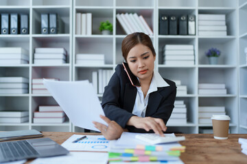 Busy businesswoman wearing a suit busy with work workaholic while sitting at work clear paperworks with documents and talk on the phone on your smartphone hear the hustle and bustle, busy concepts.