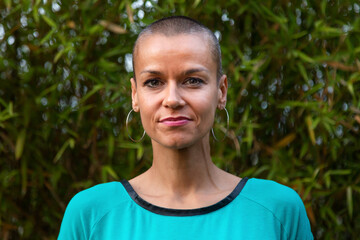 Horizontal headshot of adult caucasian woman in nature with big earring hoops and buzz haircut.