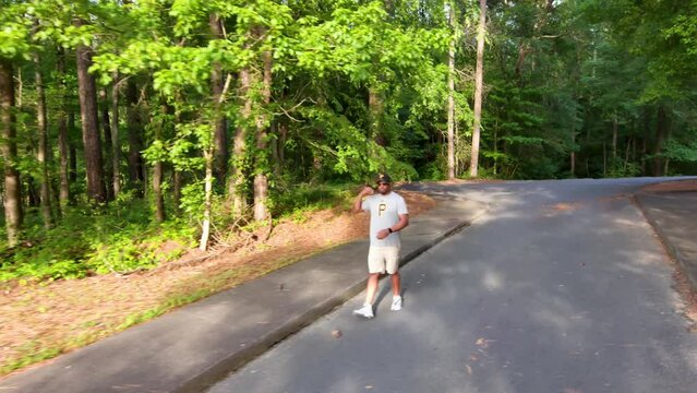 An African American man riding a Onewheel electric skateboard surrounded by lush green trees, plants and grass with parked cars at Proctor Landing Park at lake Acworth in Acworth Georgia USA