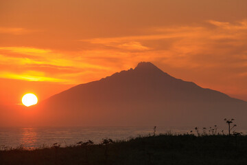 夕陽に染まる海と山影に沈む太陽
