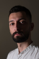 Obraz premium A young Syrian man looks at the camera in a tightly cropped portrait. The portrait is shadowy and dark, with a single light illuminating his handsome features, heavy eyes, and black beard.