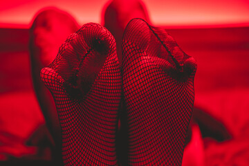 Details of sexy legs and feet in fishnet stockings in bed under seductive and intimate red light