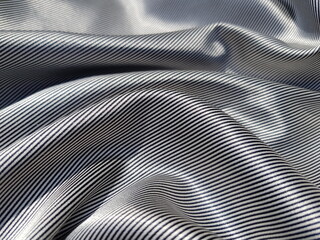 Wavy surface of silk fabric with striped black and white print, narrow strip, in folds (macro, texture).